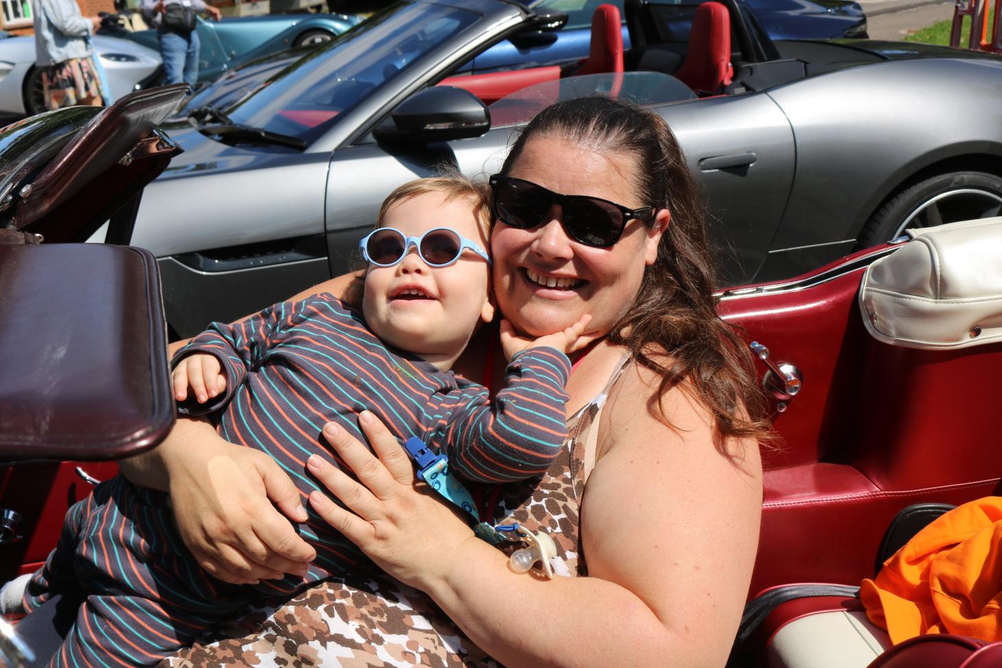 Teddie in an open-top car with his Mum. Both of them are smiling.
