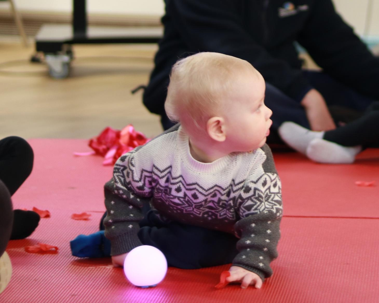 Isaac sitting up on a floor mat with a light up ball in front of him