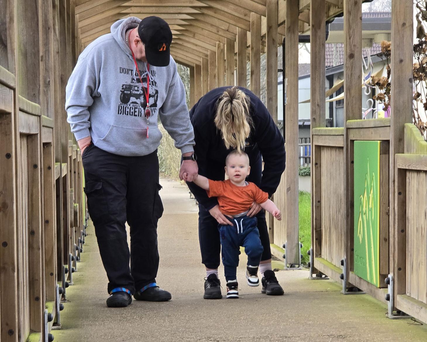 Isaac walking with help from therapist and holding dad's hand